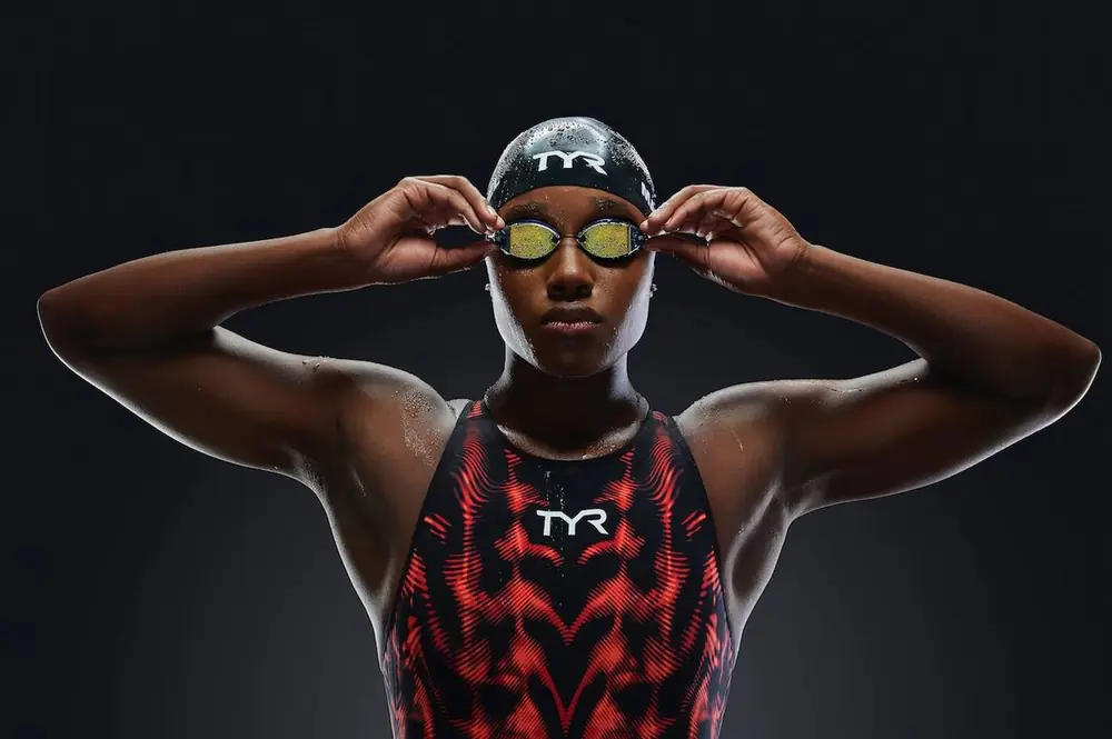 Swimmer in TYR cap and goggles against a black background
