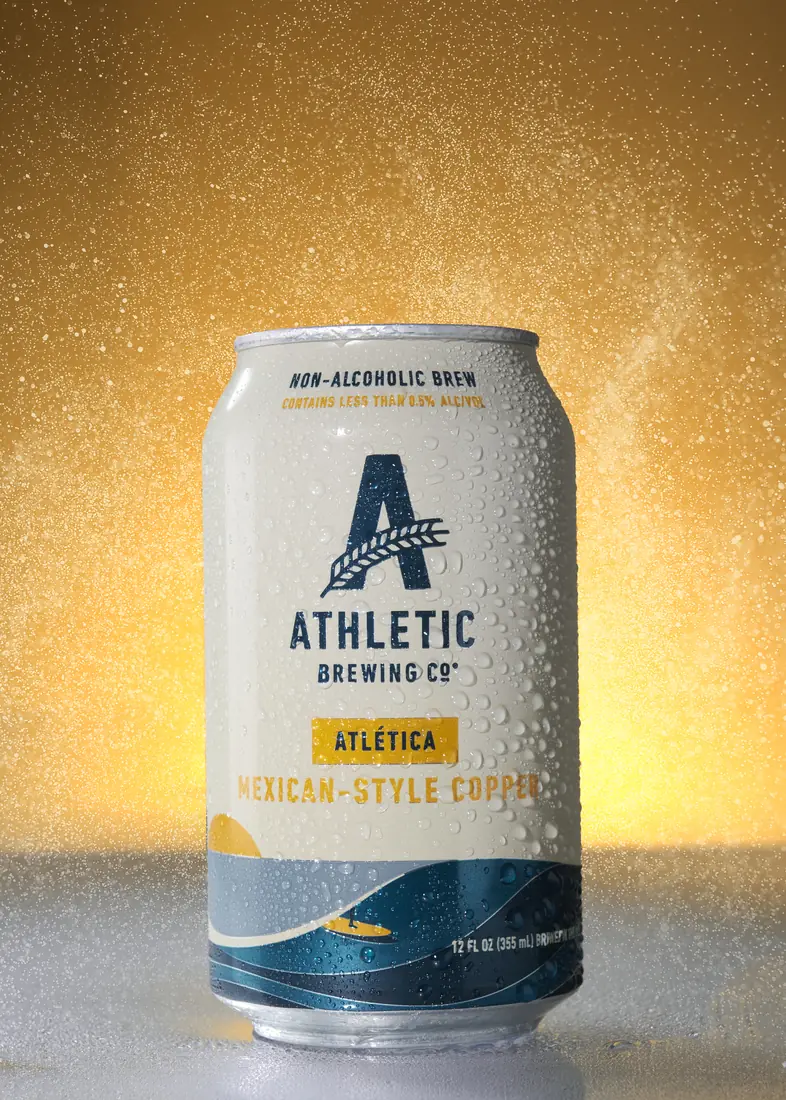 Athletic Brewing Atlética can with a gold spray backdrop