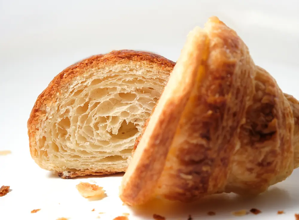 Flaky croissant halves and crumbs arranged on white