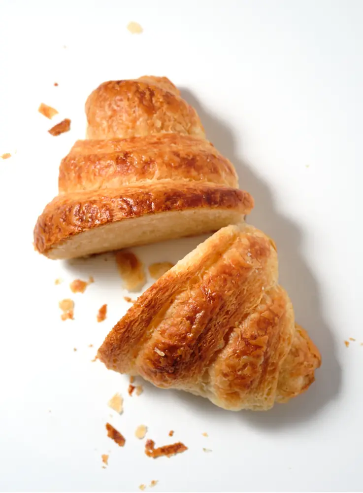 Croissant pieces and crumbs suspended across a white background