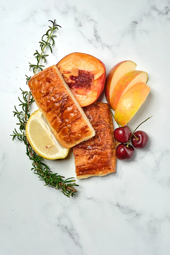 Golden pastry styled with citrus, cherries, and rosemary on stone
