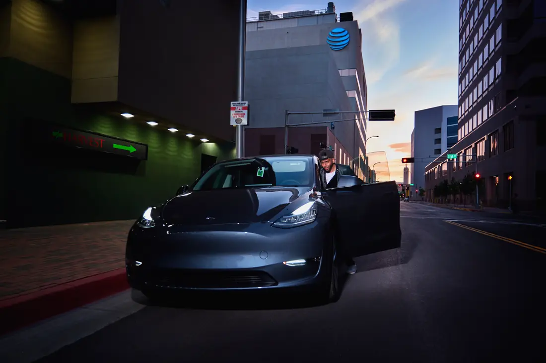 Driver beside a dark car on a downtown street at dusk