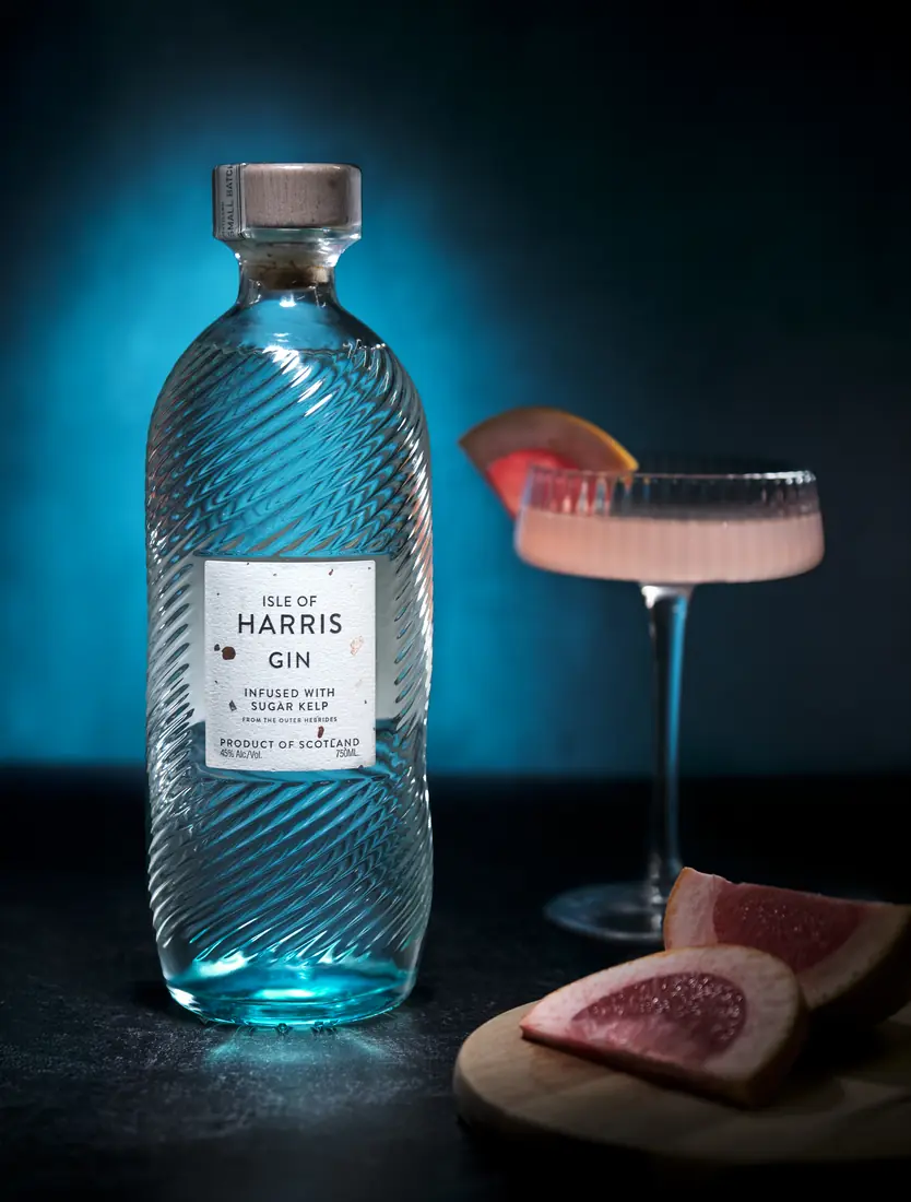 Harris Gin bottle, cocktail, and grapefruit arranged on a vivid blue set