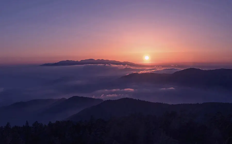 Sunrise glowing above layered mountain ridges and a sea of clouds in Nepal