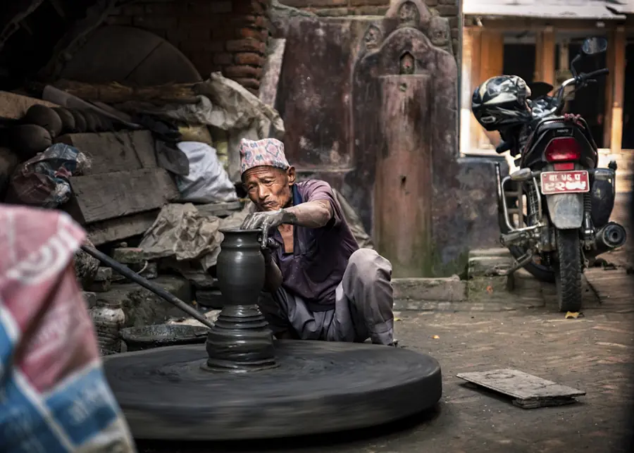 Potter working at a wheel in a textured street scene in Bhaktapur, Nepal