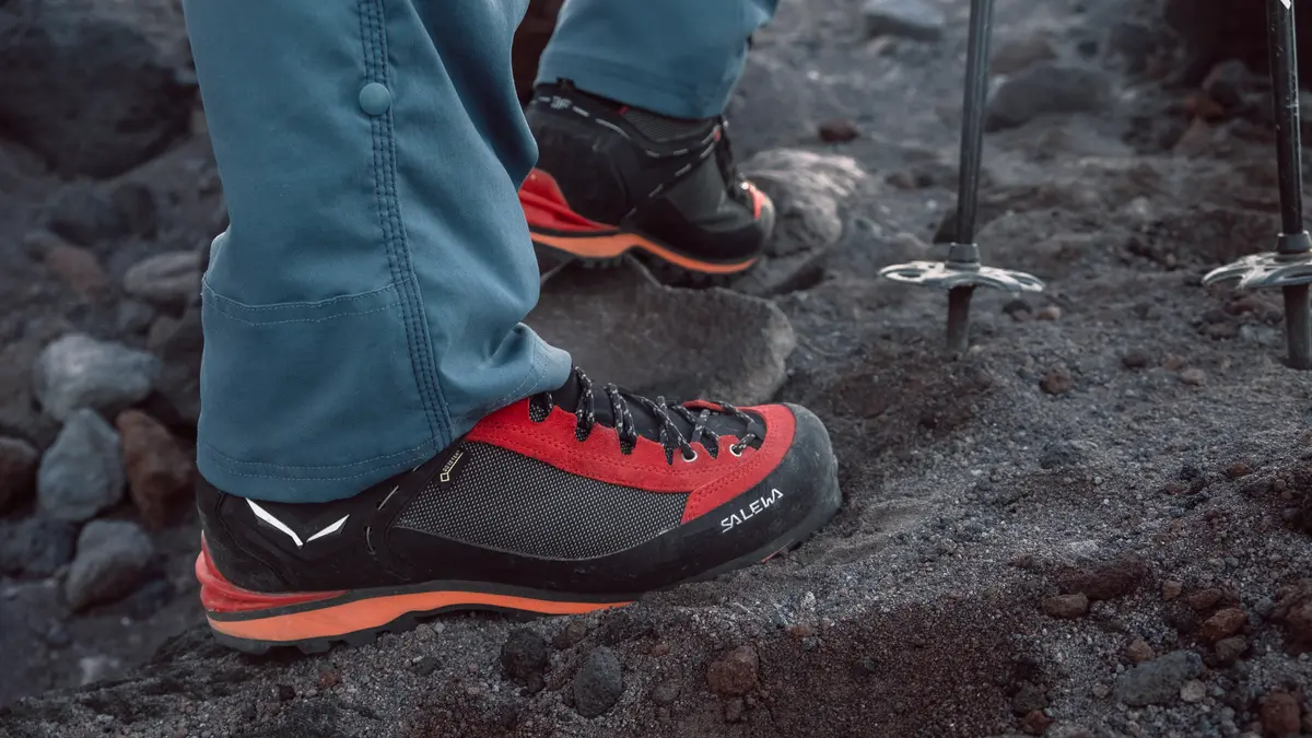 Close detail of mountain footwear and trekking poles on volcanic ground