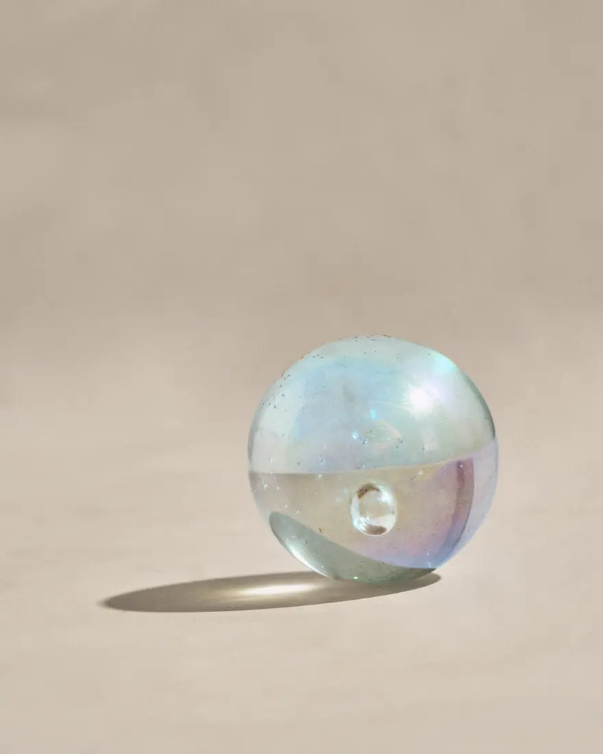 Iridescent glass orb casting a long graphic shadow on a neutral set