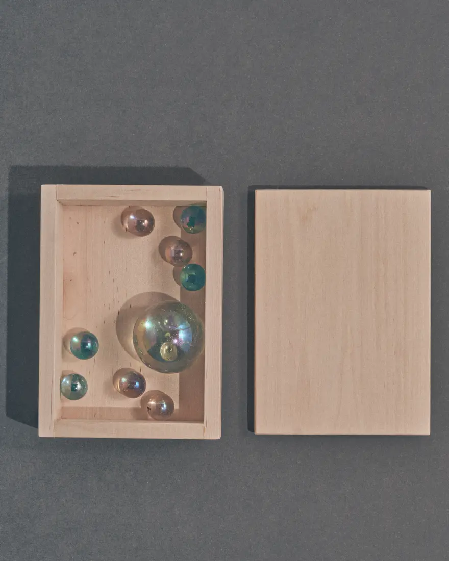 Iridescent glass spheres arranged inside a pale wooden box