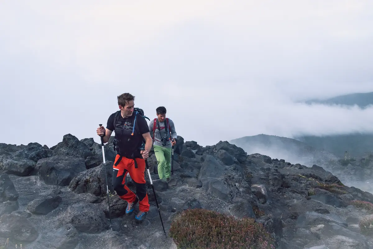 Two mountaineers climbing through dark volcanic terrain and low cloud